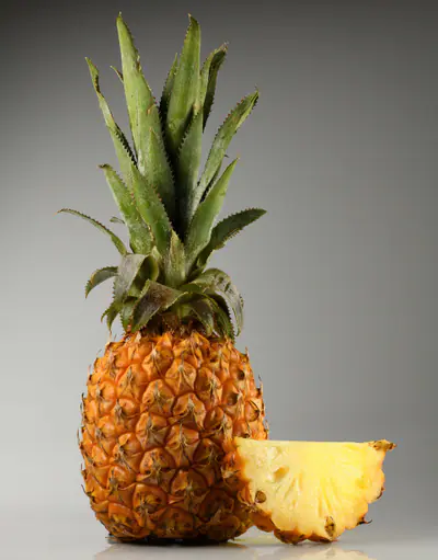 Kokonainen ananas ja siitä leikattu mehukas lohko harmaata taustaa vasten