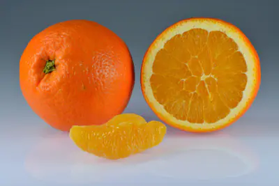 Kokonainen appelsiini, puolikas appelsiini ja kuorittu lohko harmaalla taustalla