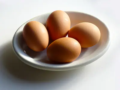 Neljä ruskeaa kananmunaa valkoisessa matalassa kulhossa vaalealla pöydällä