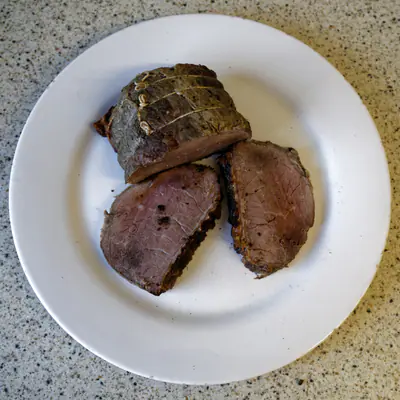 Uunissa paistettu naruun sidottu naudanpaisti ja kaksi viipaletta valkoisella lautasella