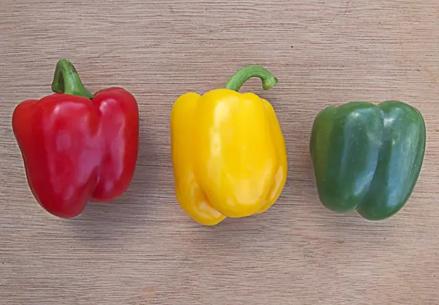 Punainen, keltainen ja vihreä paprika rivissä vaalealla puupinnalla