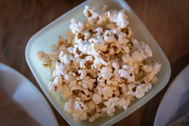 Popcornia vaaleassa neliskulmaisessa kulhossa puupöydällä ylhäältä kuvattuna