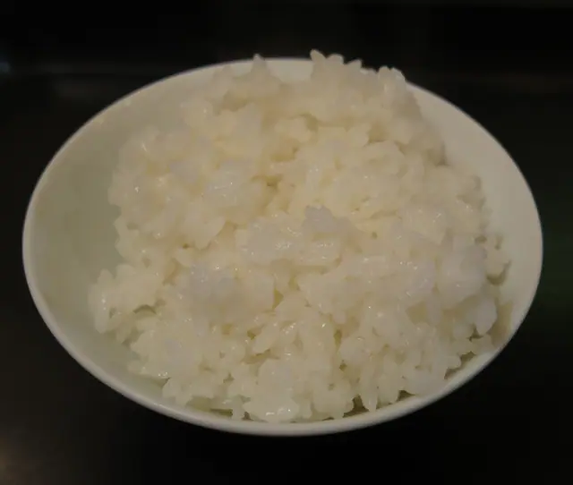 Valkoinen kulho täynnä keitettyä valkoista riisiä tummaa taustaa vasten