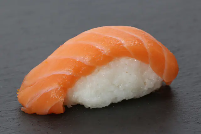 Lohinigiri: sushiriisipala tuoreen lohiviipaleen alla tummalla liuskekivialustalla