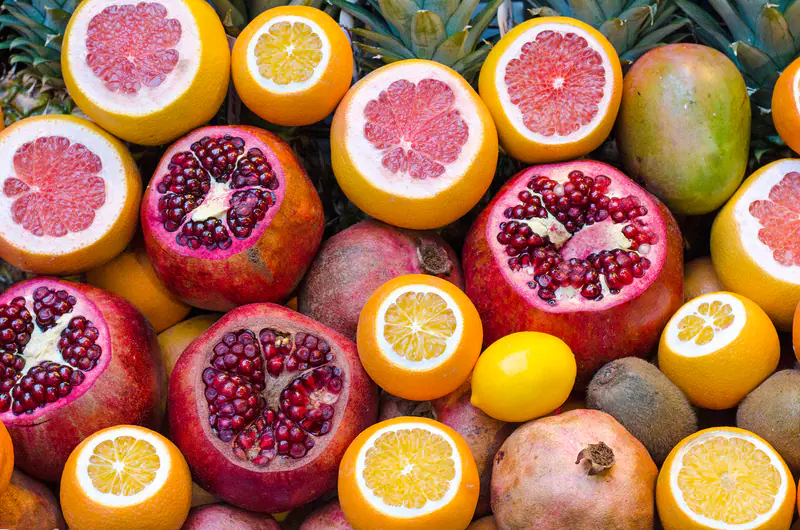 Halkaistuja greippejä ja appelsiineja, avattuja granaattiomenoita, sitruuna, mango ja kiivejä tiiviissä kasassa